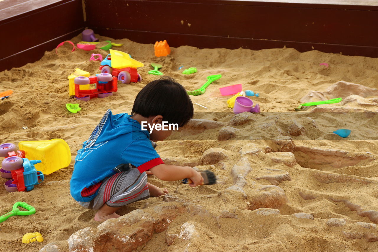 Side view of boy playing with toys on sand