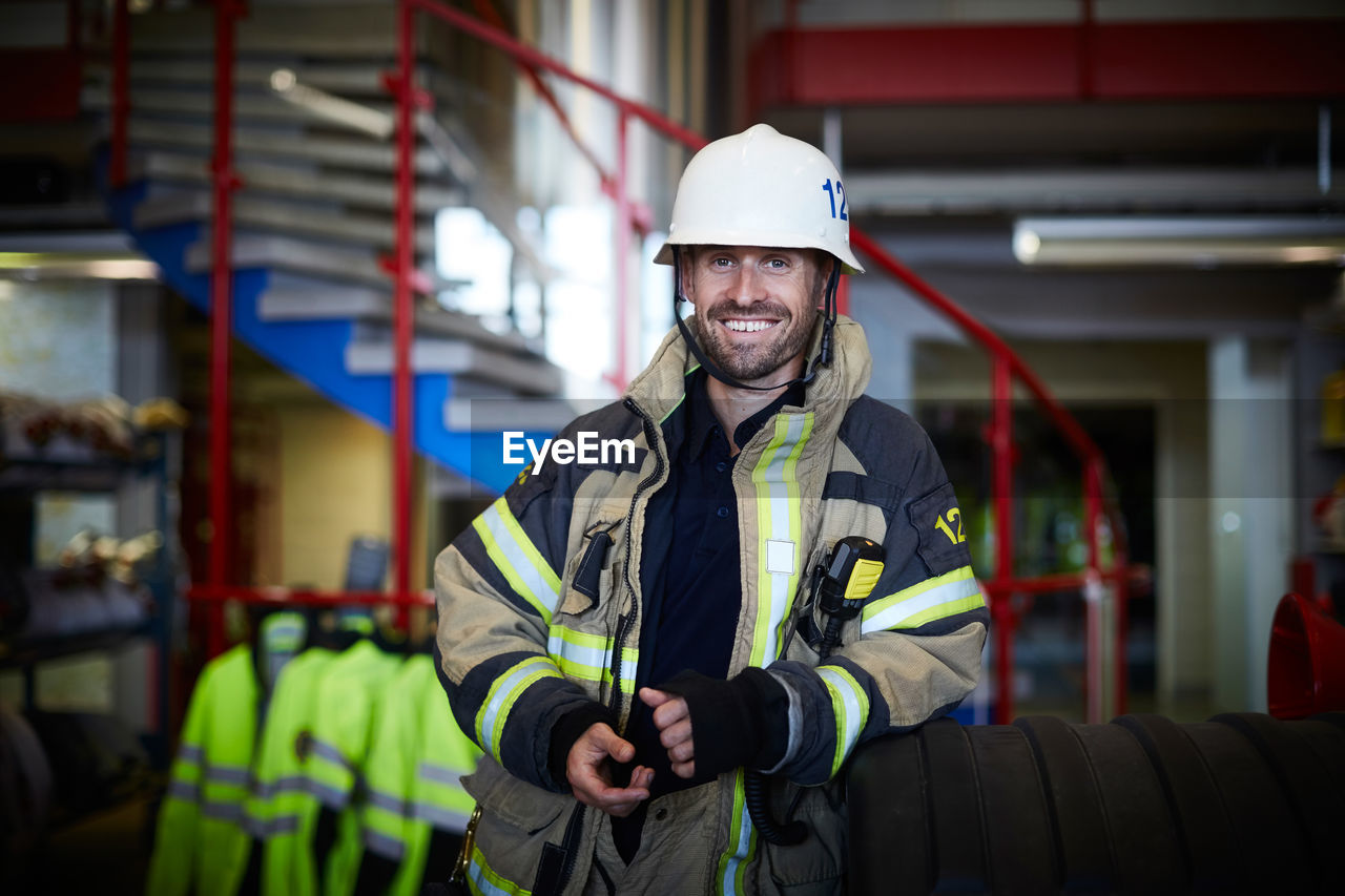 Portrait of smiling firefighter wearing protective suit at fire station