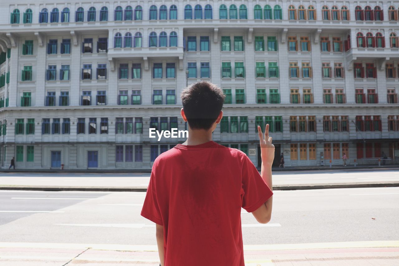 REAR VIEW OF MAN STANDING ON STREET AGAINST BUILDING