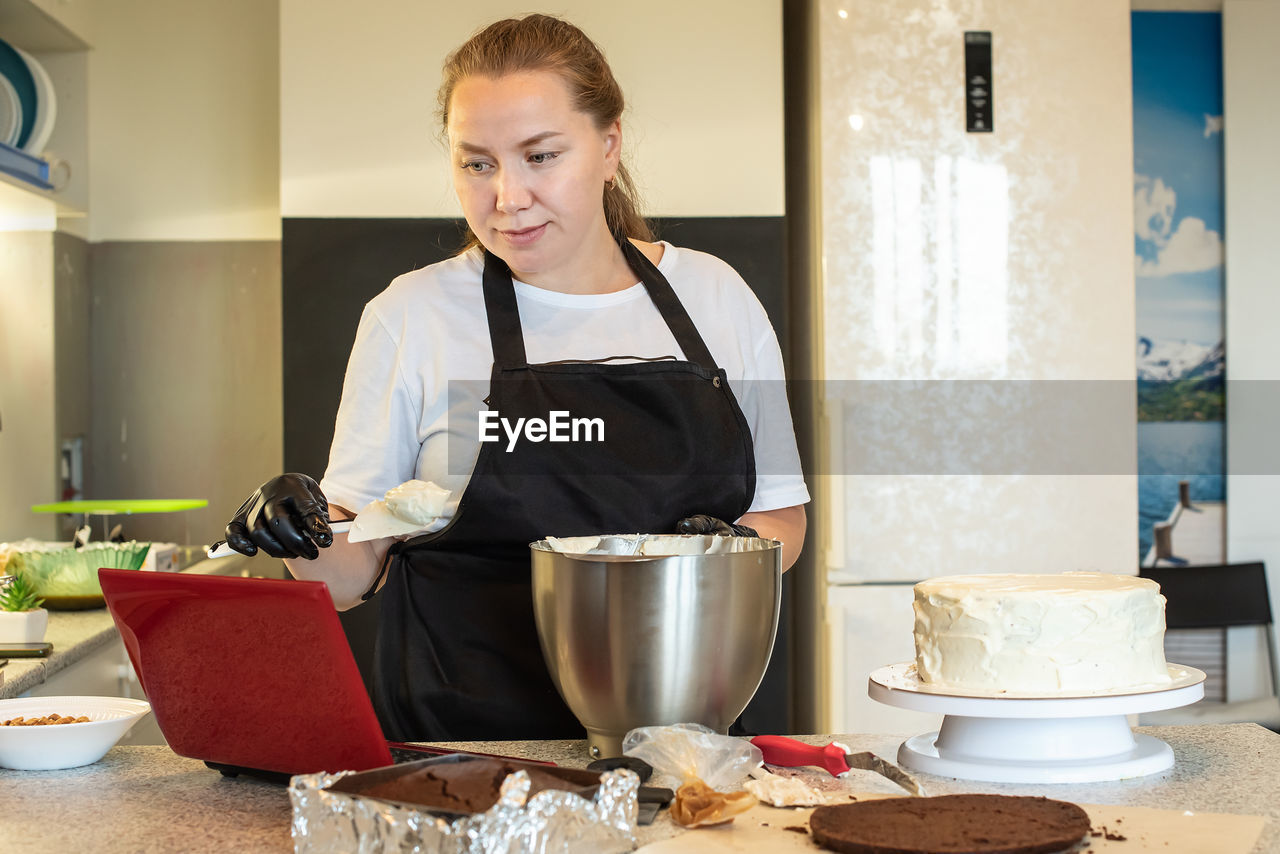 Blogger pastry chef cook confectioner  makes a cake. woman in apron using notebook while cooking.