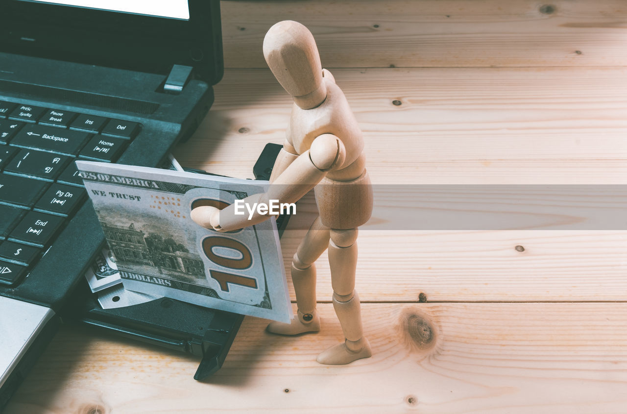 High angle view of figurine holding paper currency by laptop on table