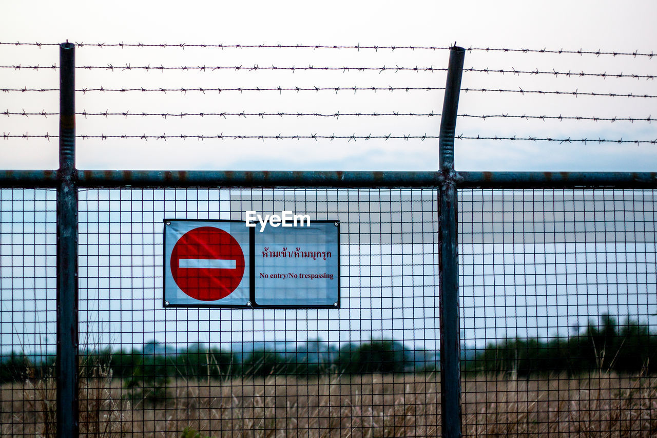 Sign on fence against sky