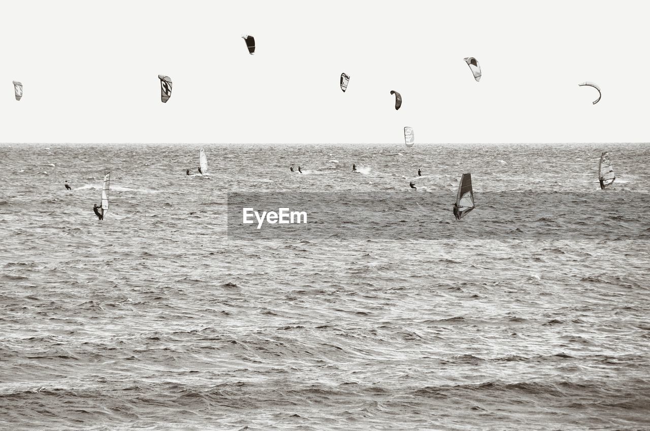 People enjoying parasailing and wind surfing over sea against clear sky