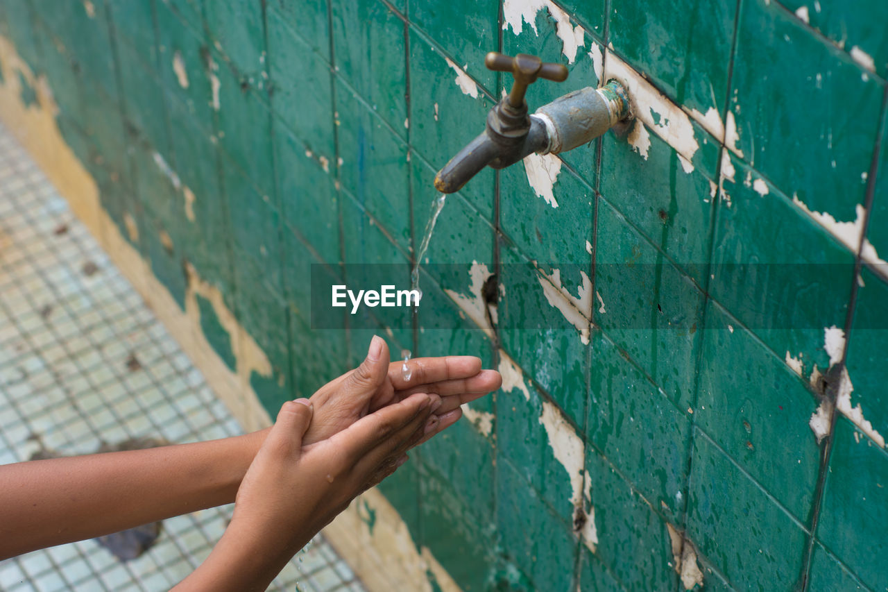 Cropped image of person washing hands in running water outdoors