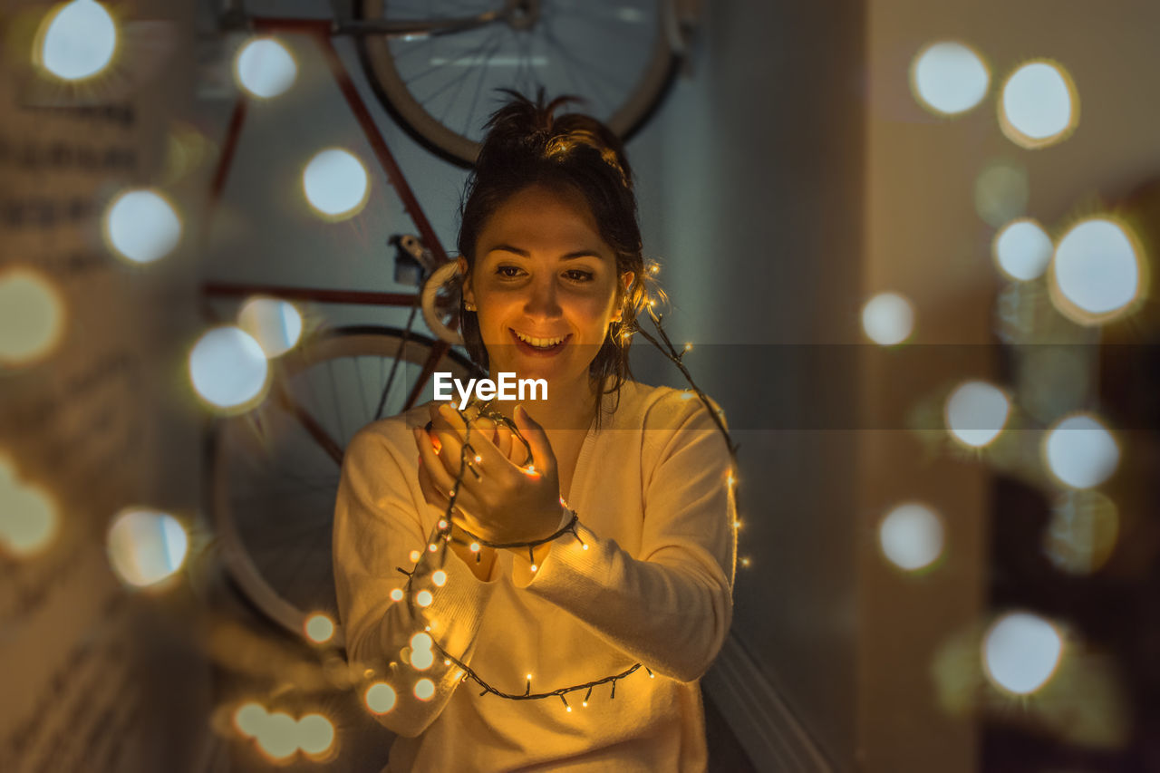 Smiling young woman holding illuminated string lights