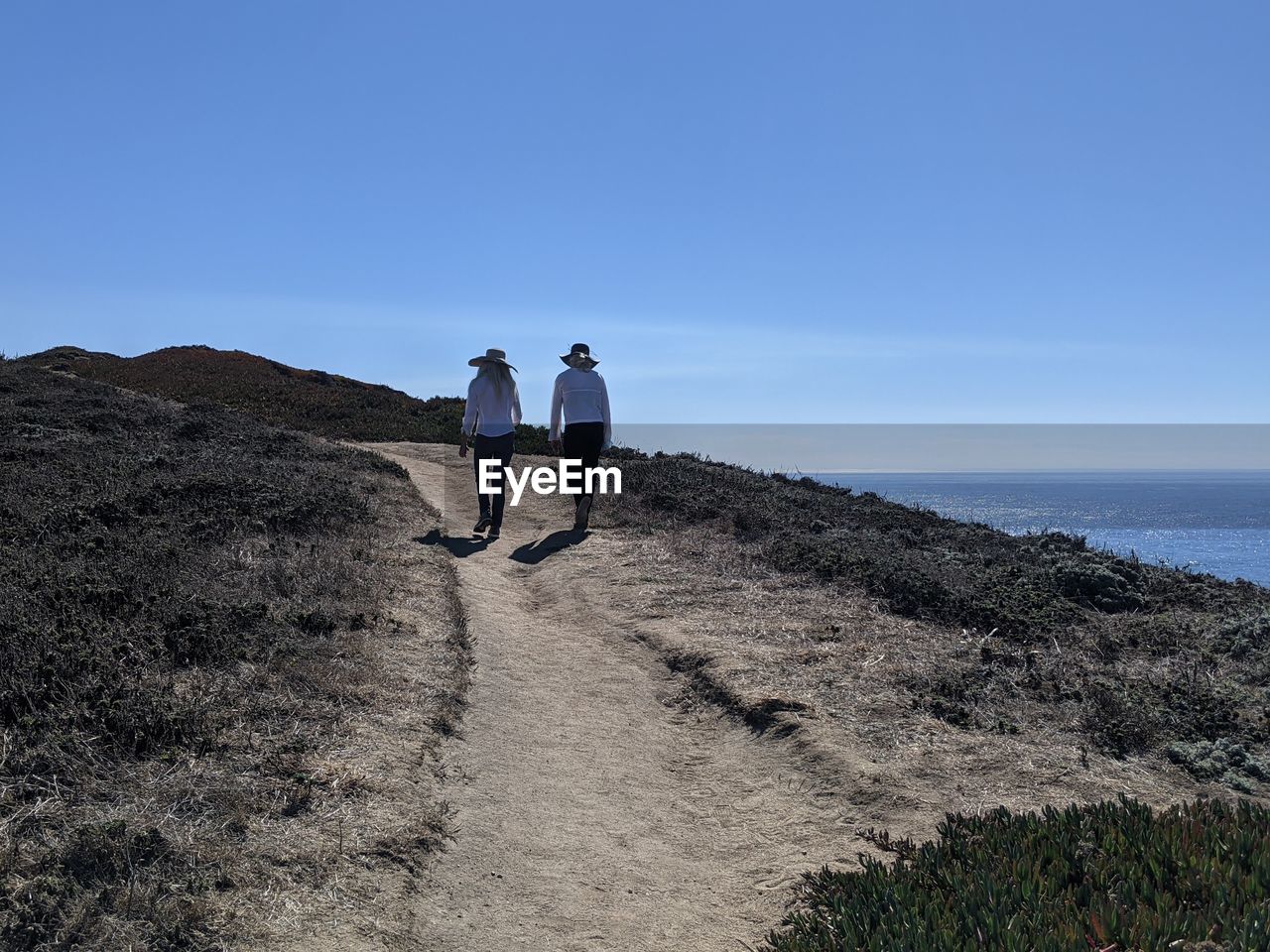 Therapeutic nature. two women walking dirt path along ocean cliffs.