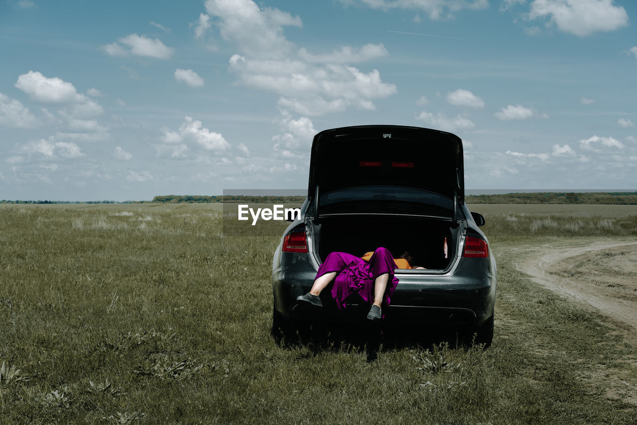 Low section of young woman in car trunk on landscape