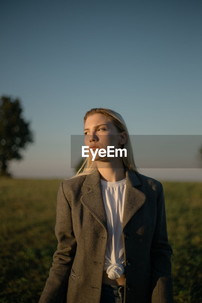 Young woman looking away on field against clear sky