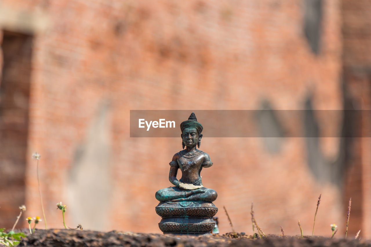Buddha sitting on serpent figurine with temple ruins on the background