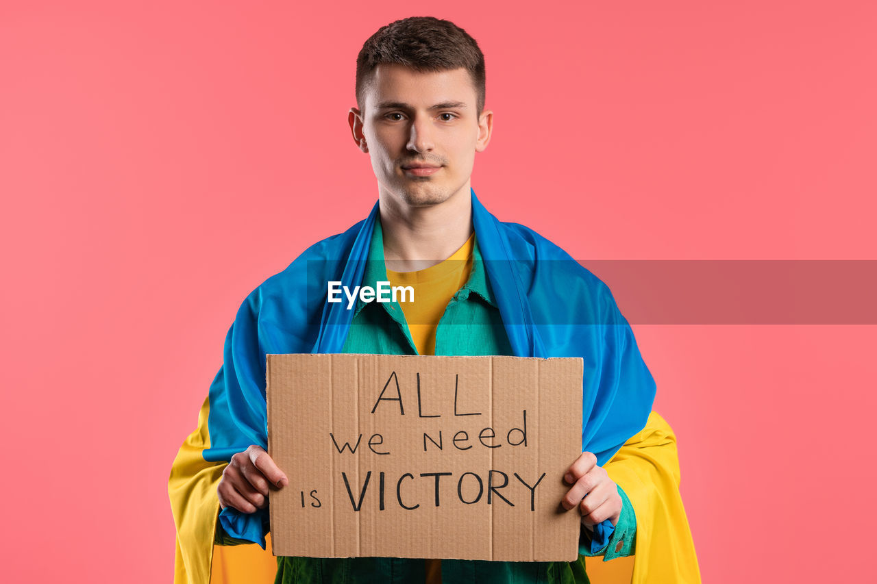 one person, portrait, studio shot, looking at camera, colored background, young adult, adult, men, text, person, clothing, holding, indoors, front view, copy space, waist up, standing, occupation, communication, emotion, sign, western script