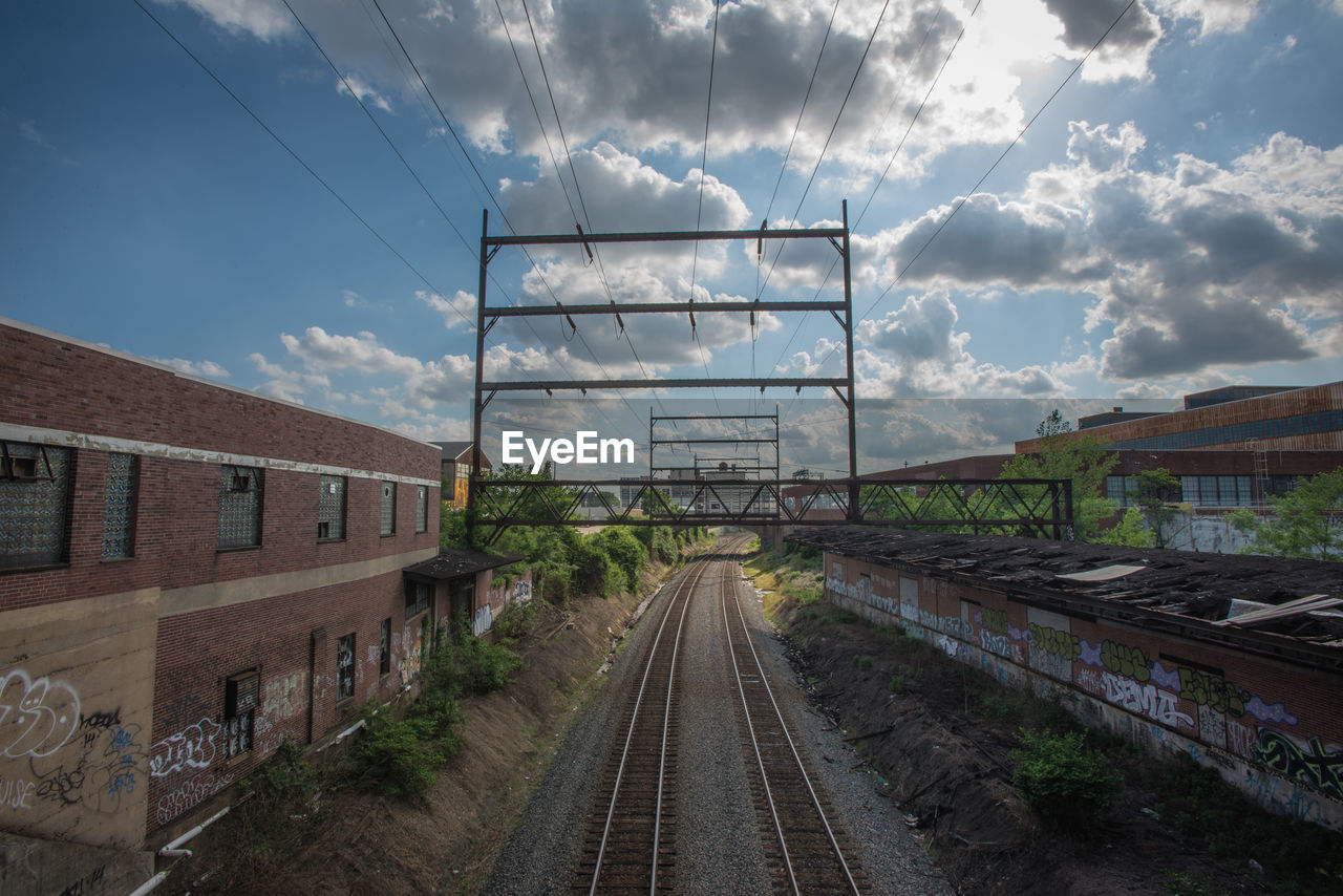 Electricity pylon over railroad track against cloudy sky