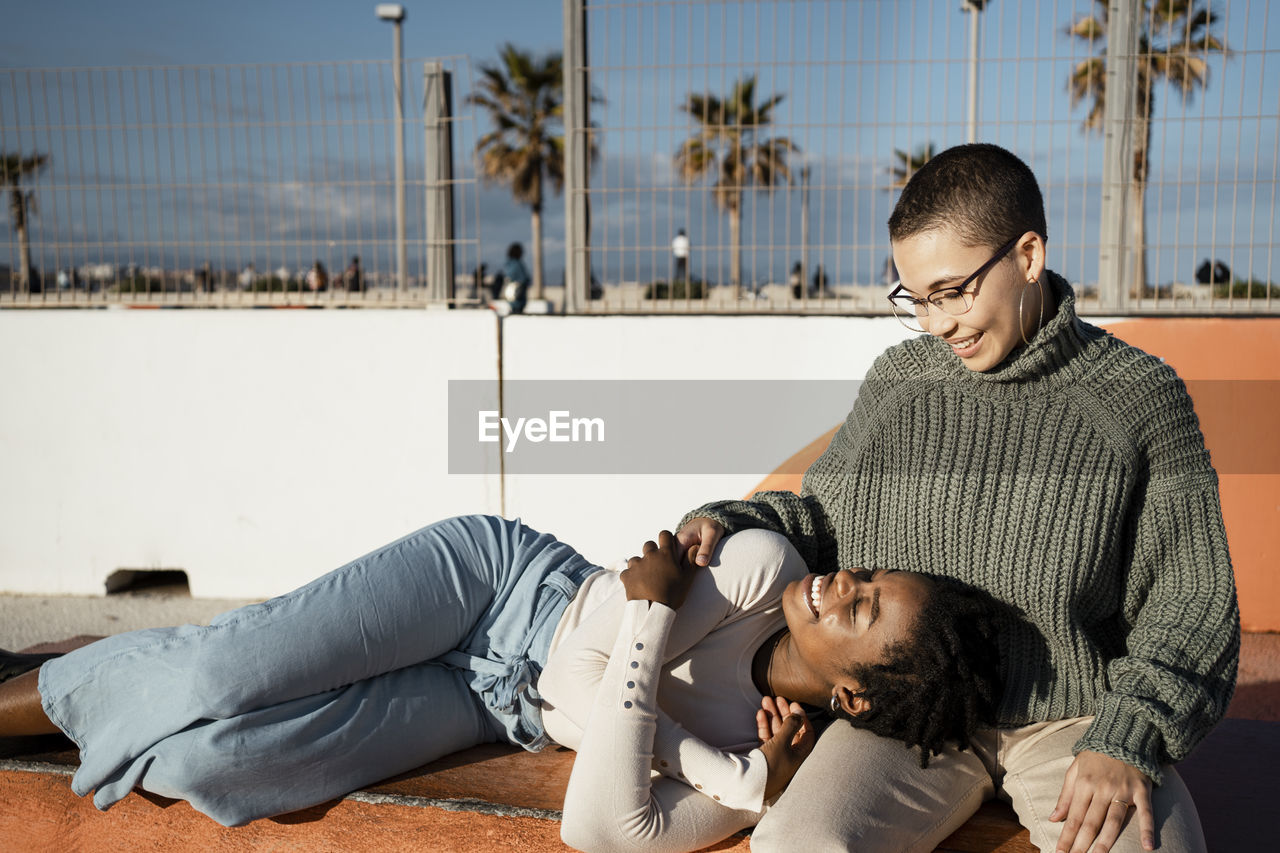 Young woman lying on friends lap while sitting on bench