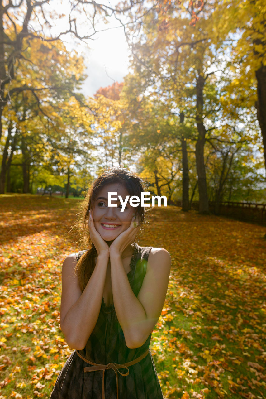 PORTRAIT OF A SMILING YOUNG WOMAN STANDING IN AUTUMN