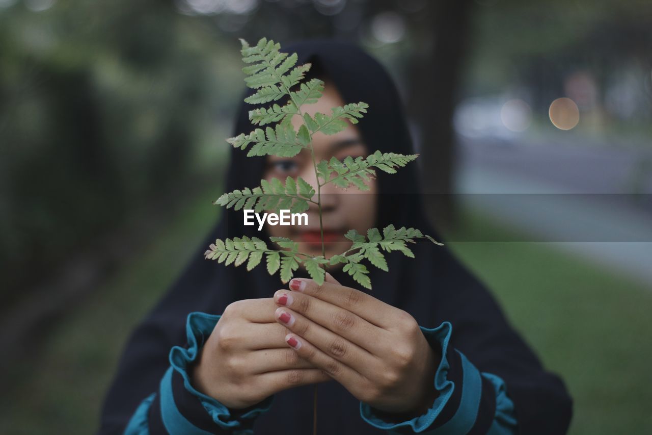 Portrait of woman holding leaves over face