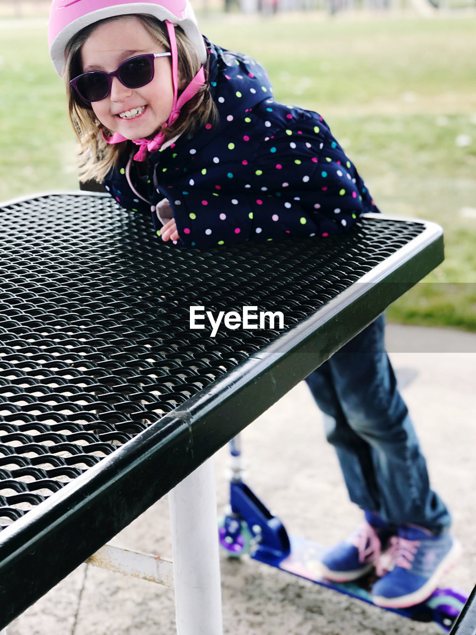 Portrait of girl smiling while standing on push scooter at table