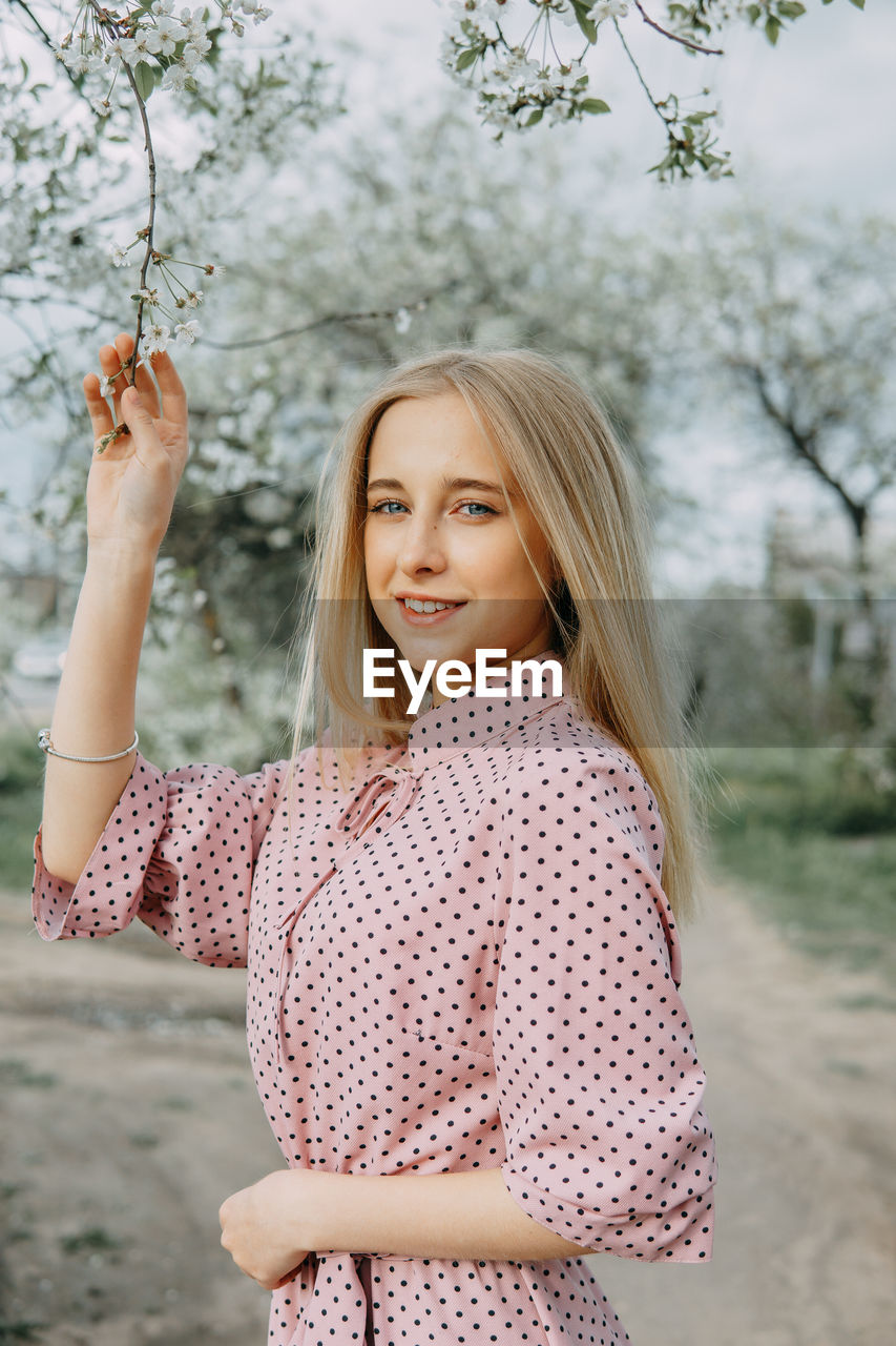 Blonde girl on a spring walk in the garden with cherry blossoms. female portrait, close-up. 