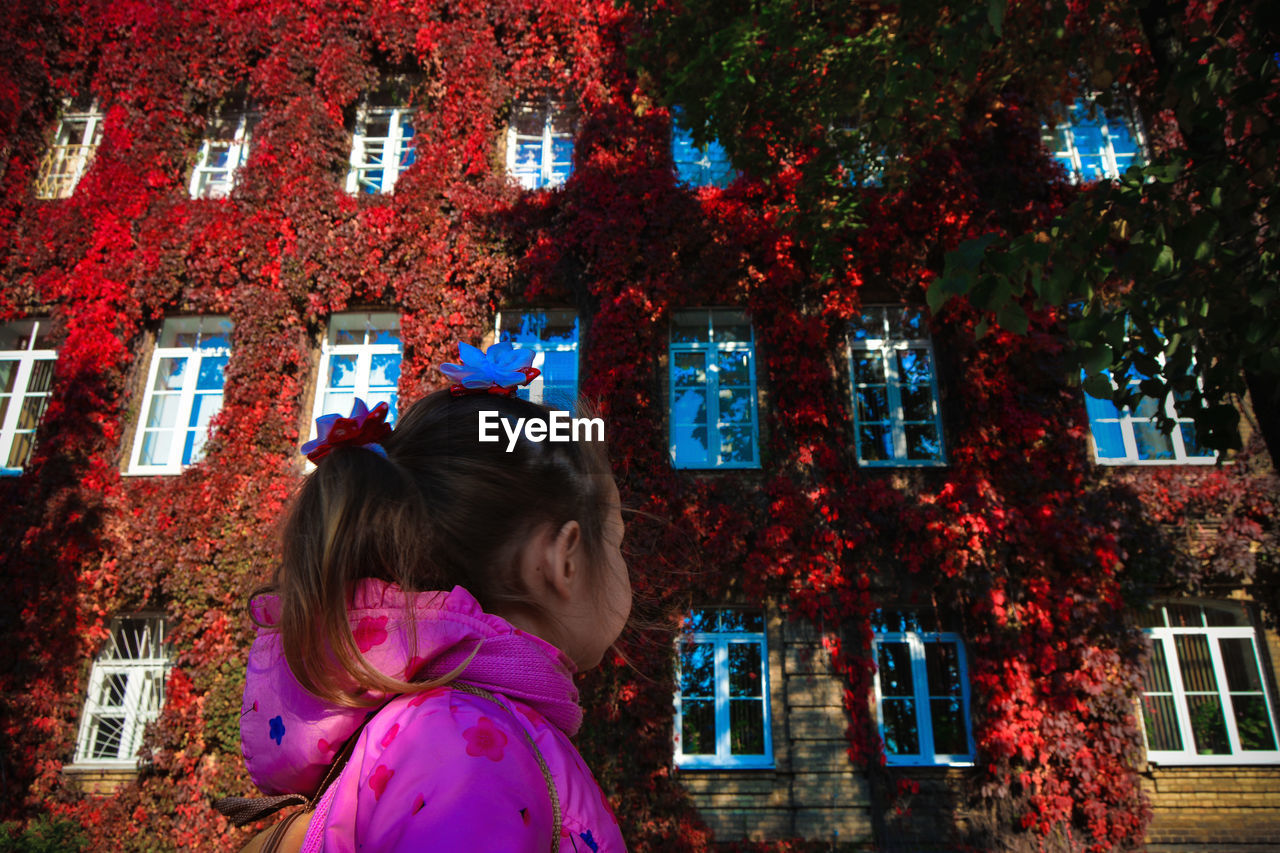Low angle view of girl looking at ivies on building during autumn