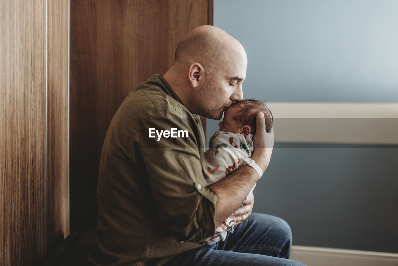 Side view of happy father kissing newborn boy in hospital