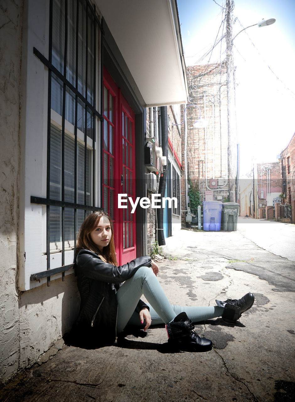 Full length portrait of woman sitting by building