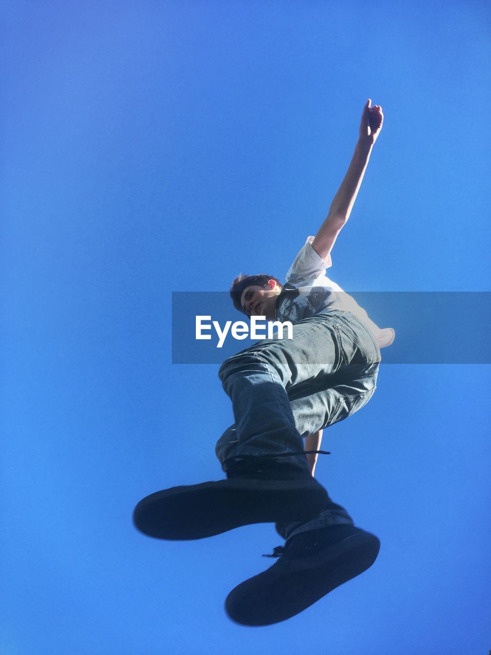 Low angle view of young man jumping against clear blue sky