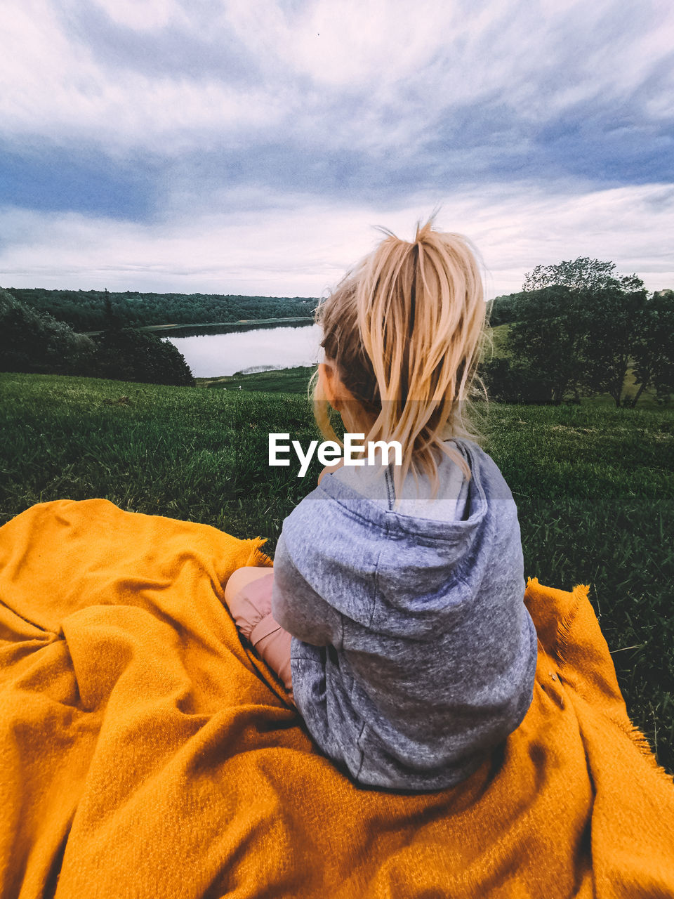 Rear view of girl sitting on yellow blanket against sky