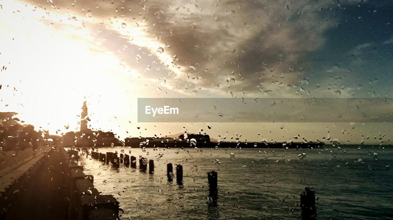 Sea and road against cloudy sky seen from wet glass window during rainy season