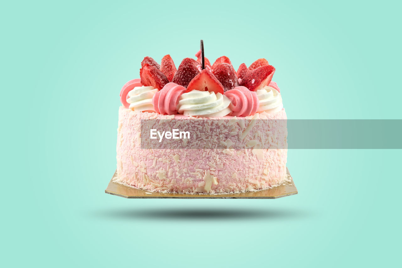 Close up of a birthday cake topped with strawberries isolated a pastel color background.