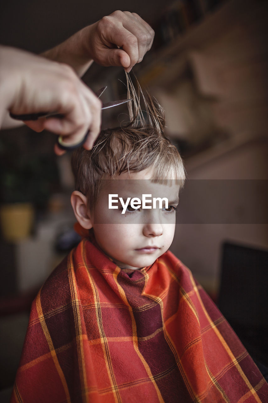 Middle aged father cutting hair to his son by himself at home looking video broadcast on laptop