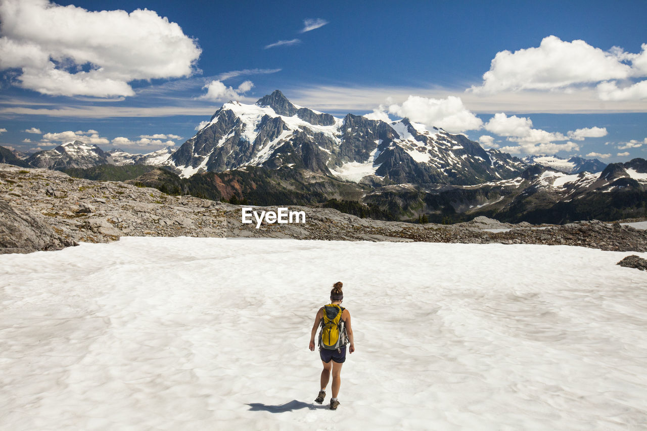 Rear view of female hiker walking on snow against mountains and cloudy sky during winter at north cascades national park