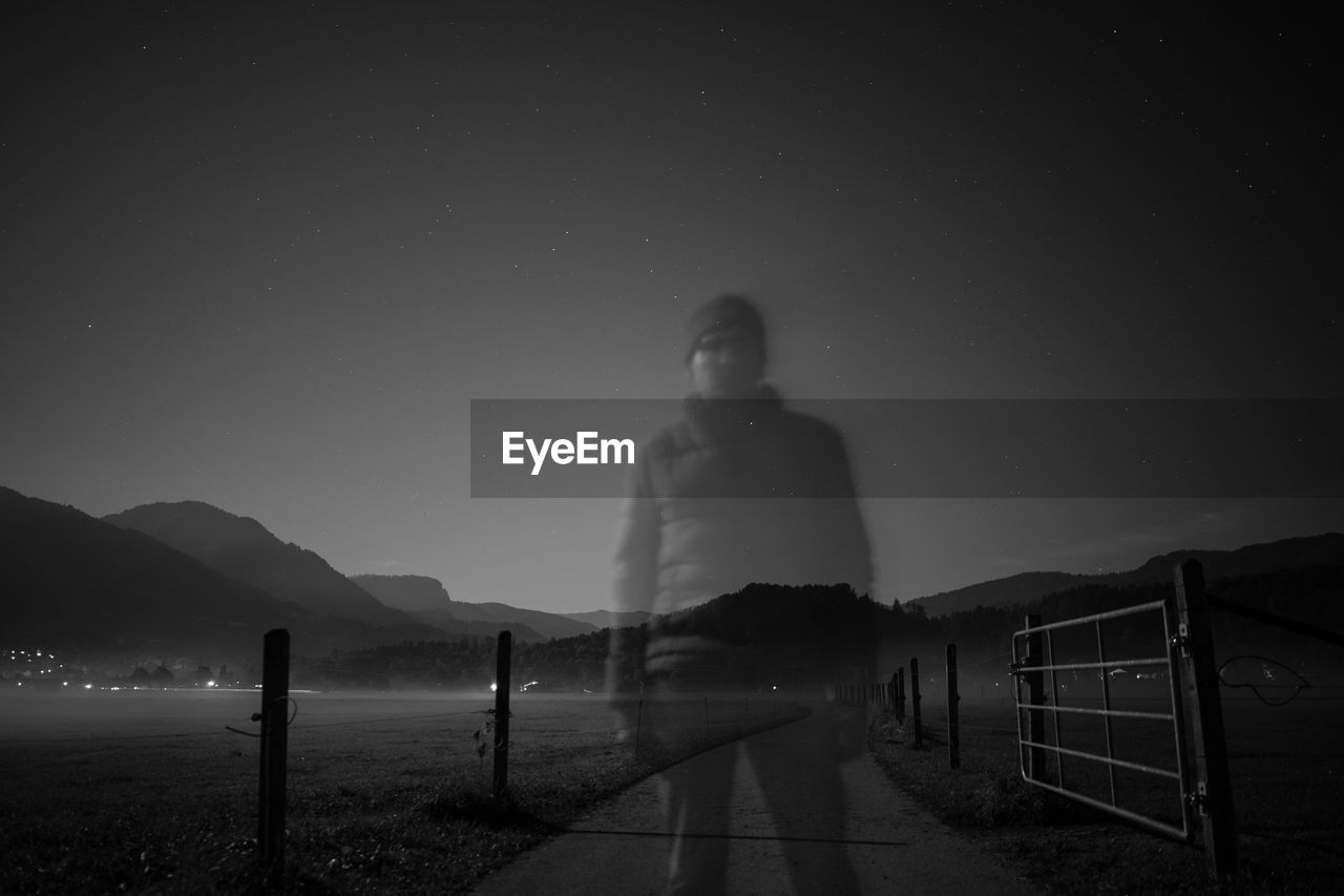 MAN STANDING BY FENCE AGAINST SKY