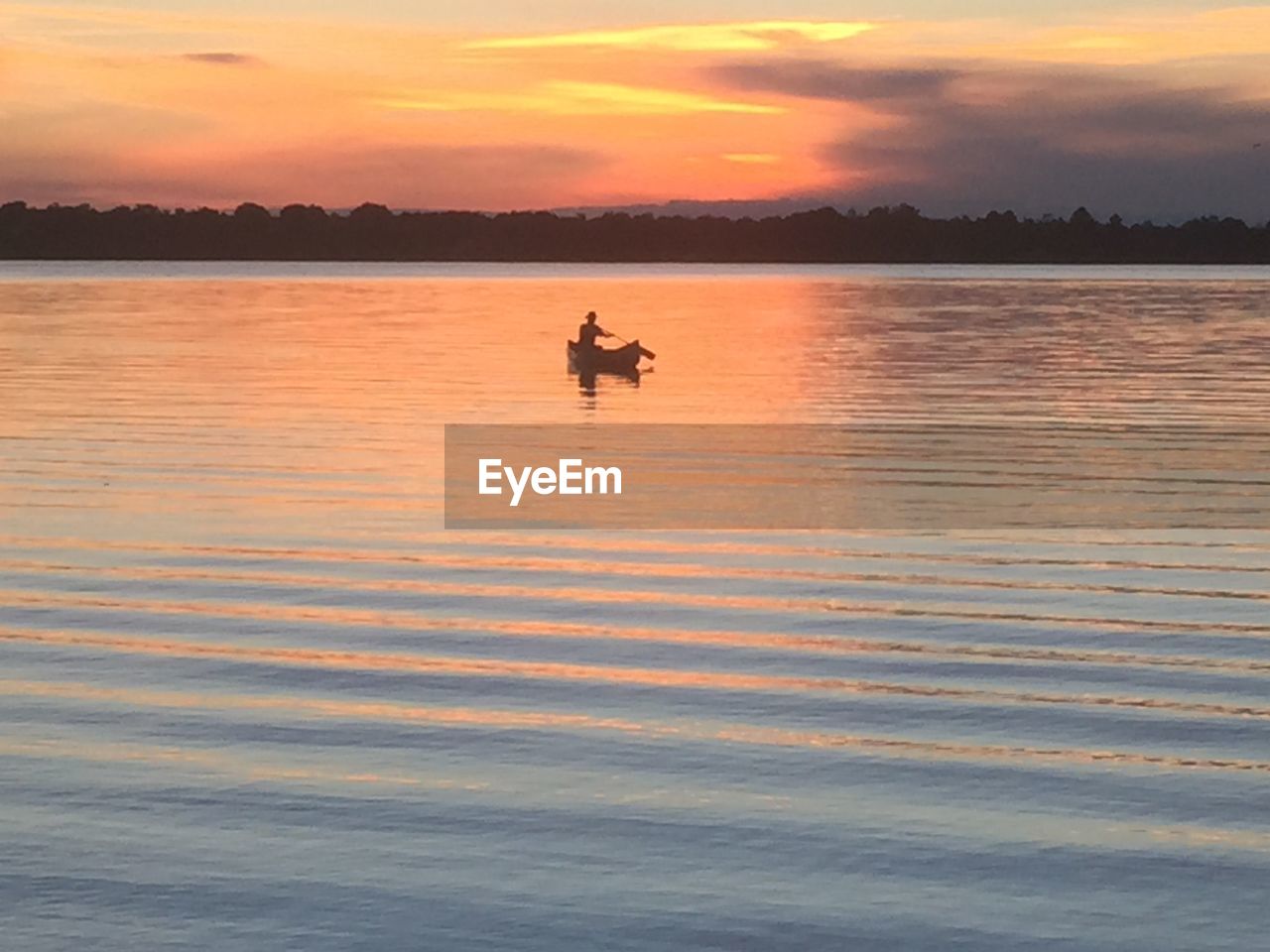 Person rowing boat in river during sunset