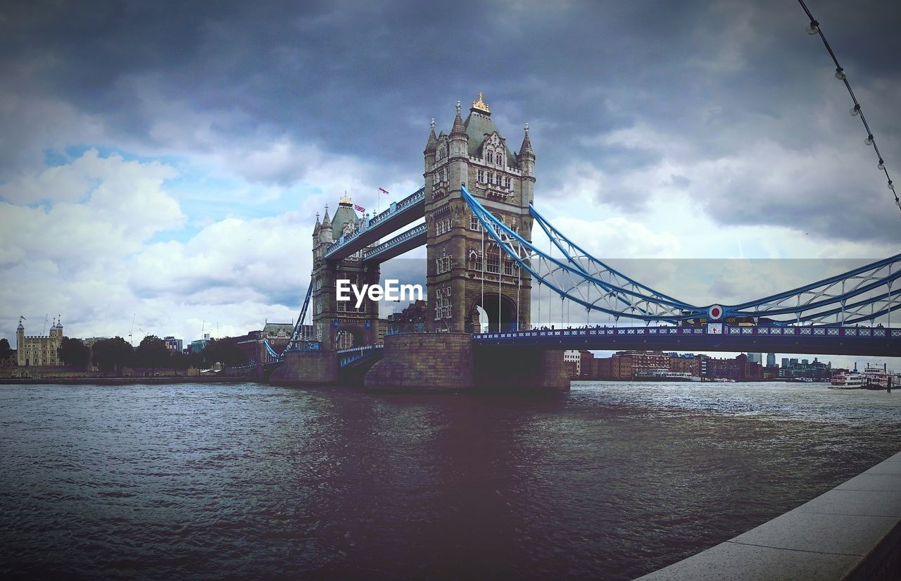 Low angle view of bridge over river against cloudy sky