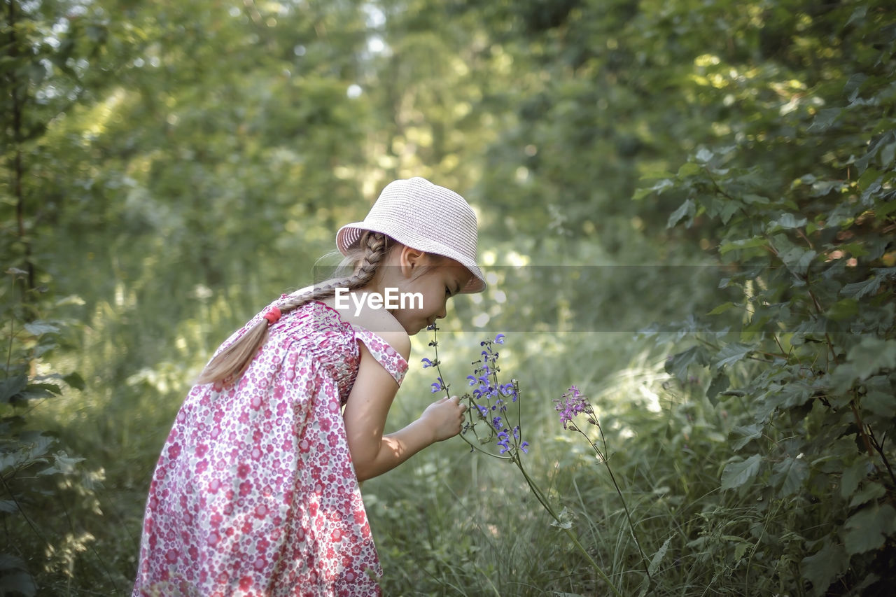 Side view of girl wearing hat standing against plants