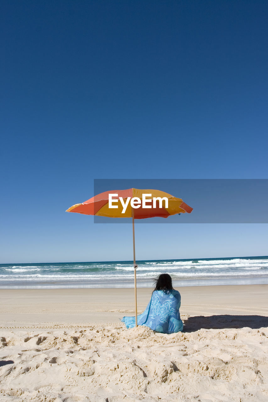 Rear view of woman relaxing on beach against sky