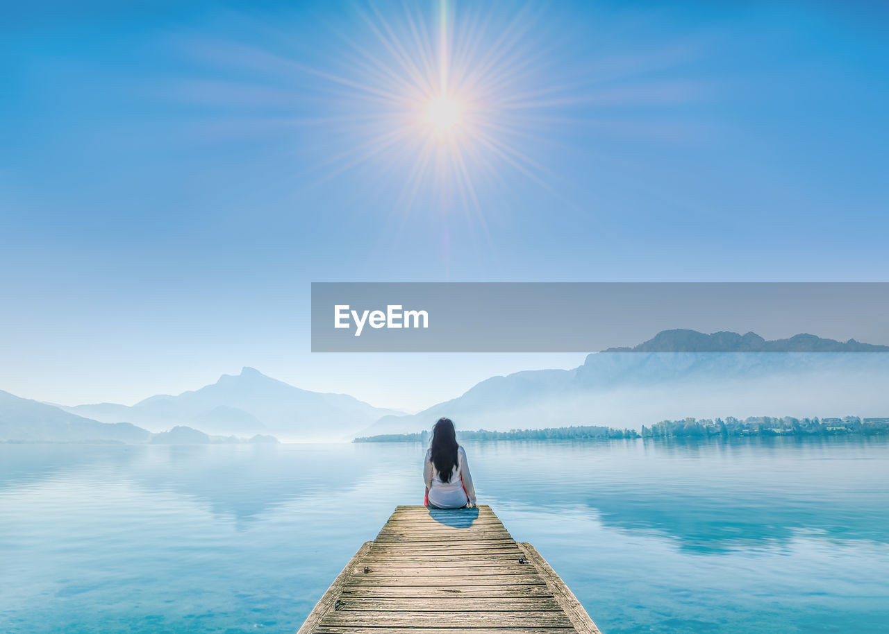 Rear view of woman on pier at lake against sky