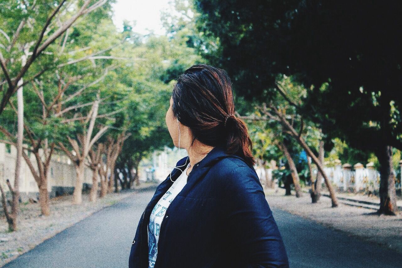 Woman standing on road amidst trees