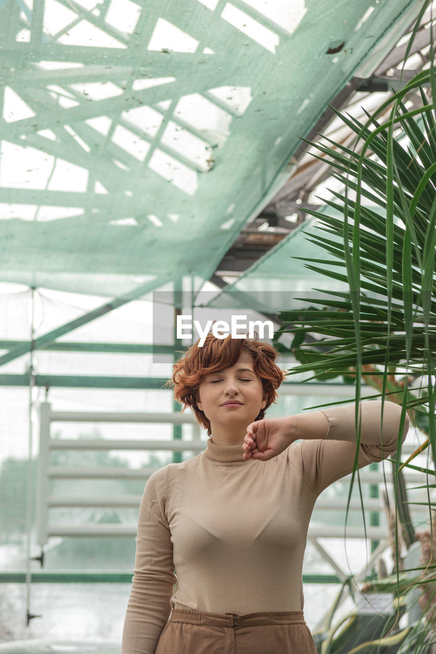 A beautiful plus size girl enjoying standing among the green plants of the greenhouse.