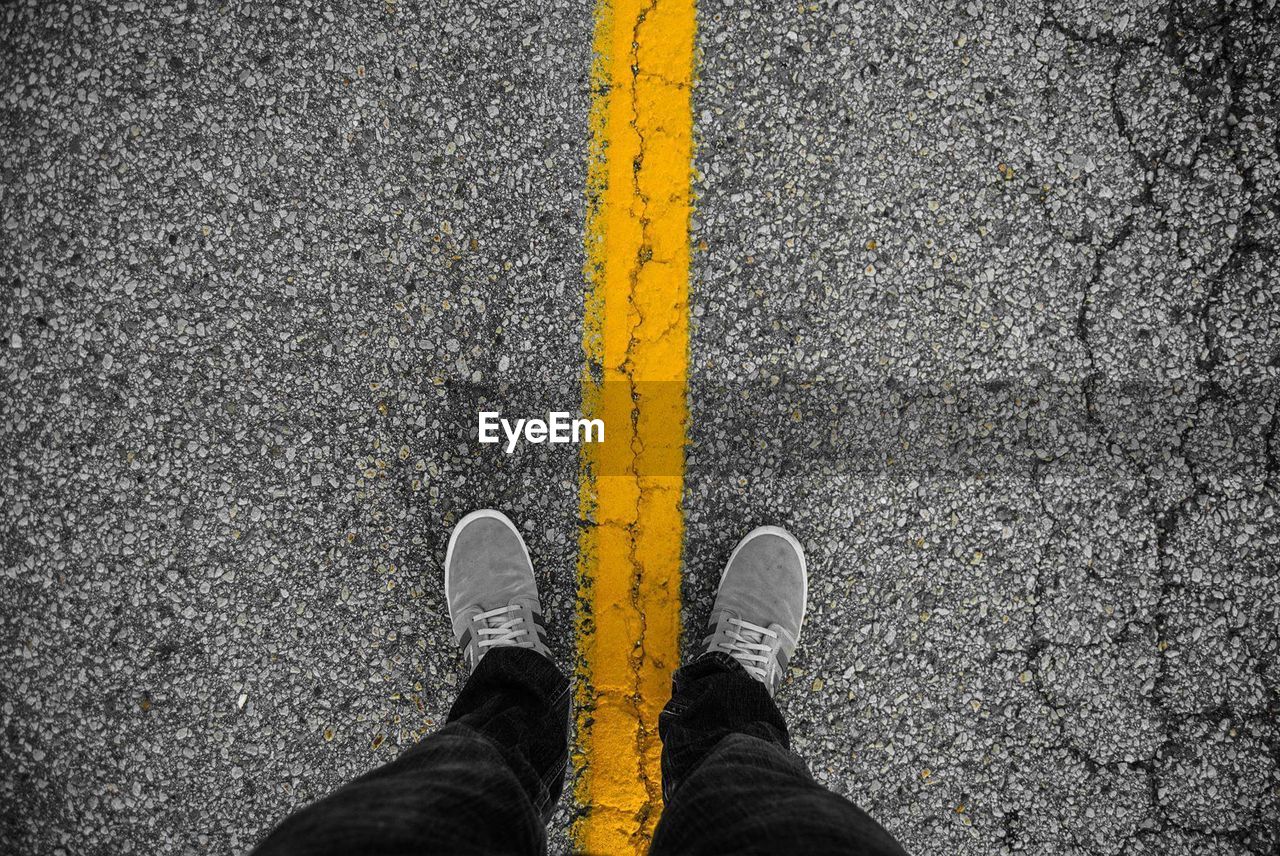 Low section view of person standing on yellow line of road