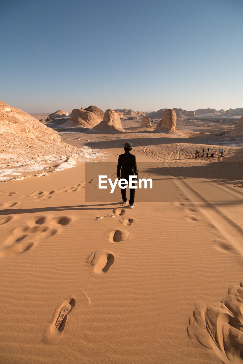 Full length rear view of man walking in desert against clear sky