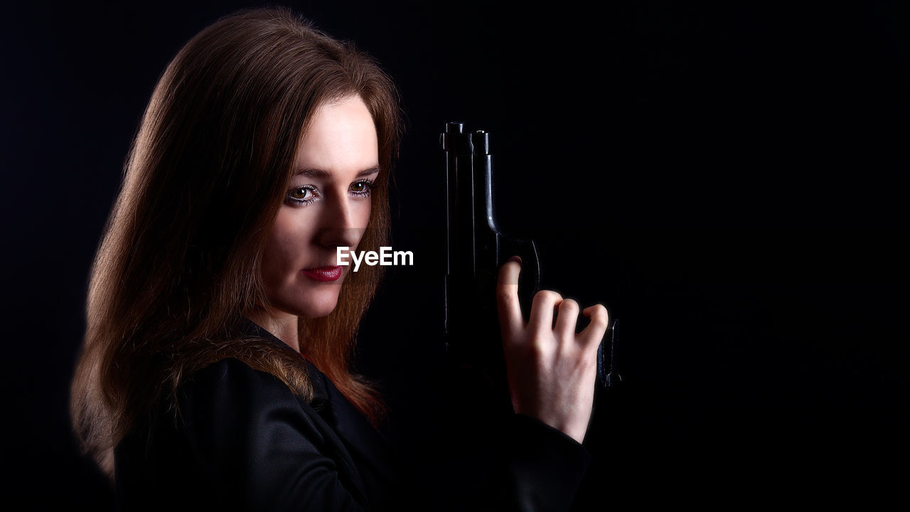 Woman looking away while holding gun against black background