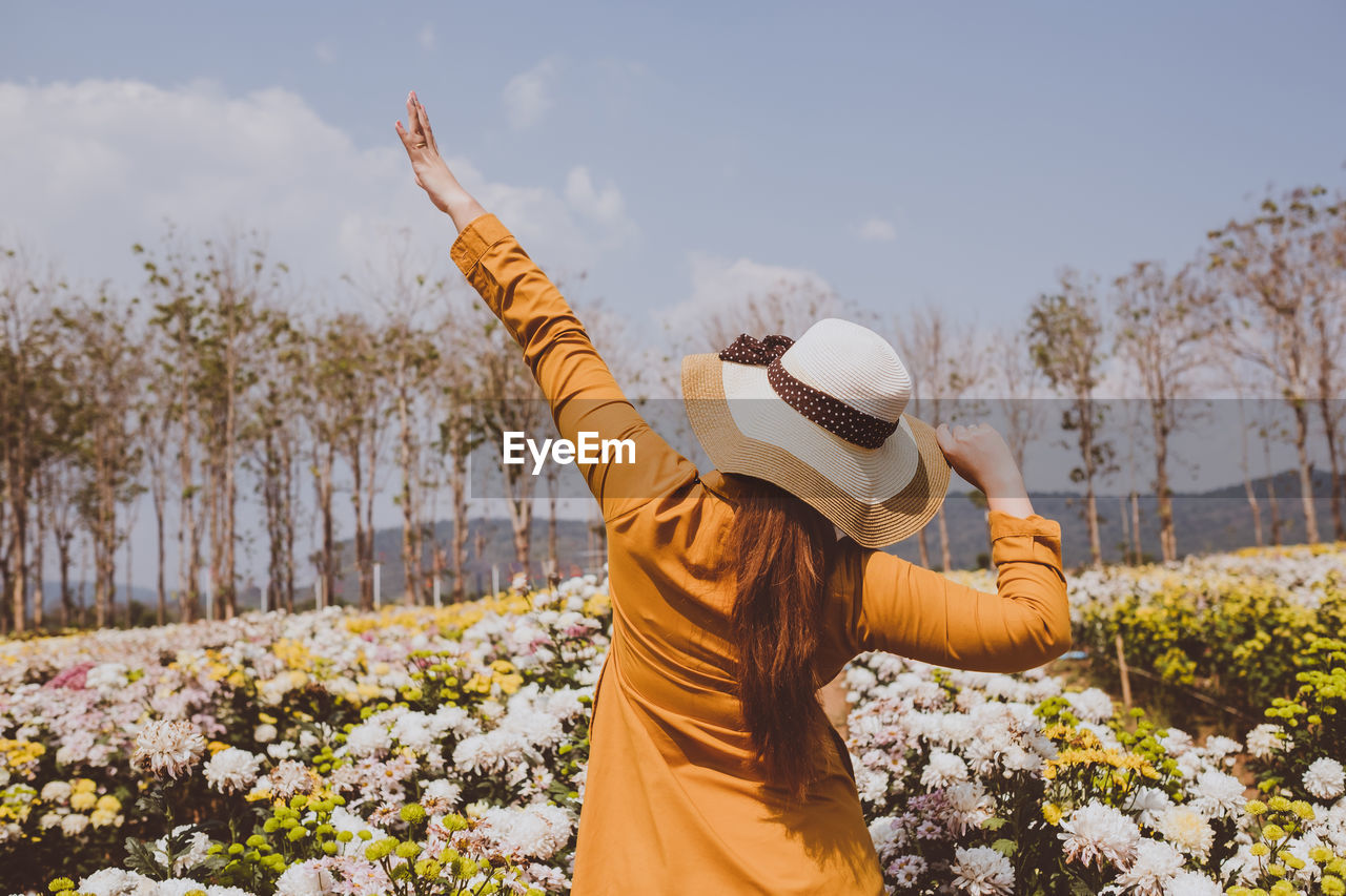 Rear view of woman with arms raised standing by flowering plants at farm