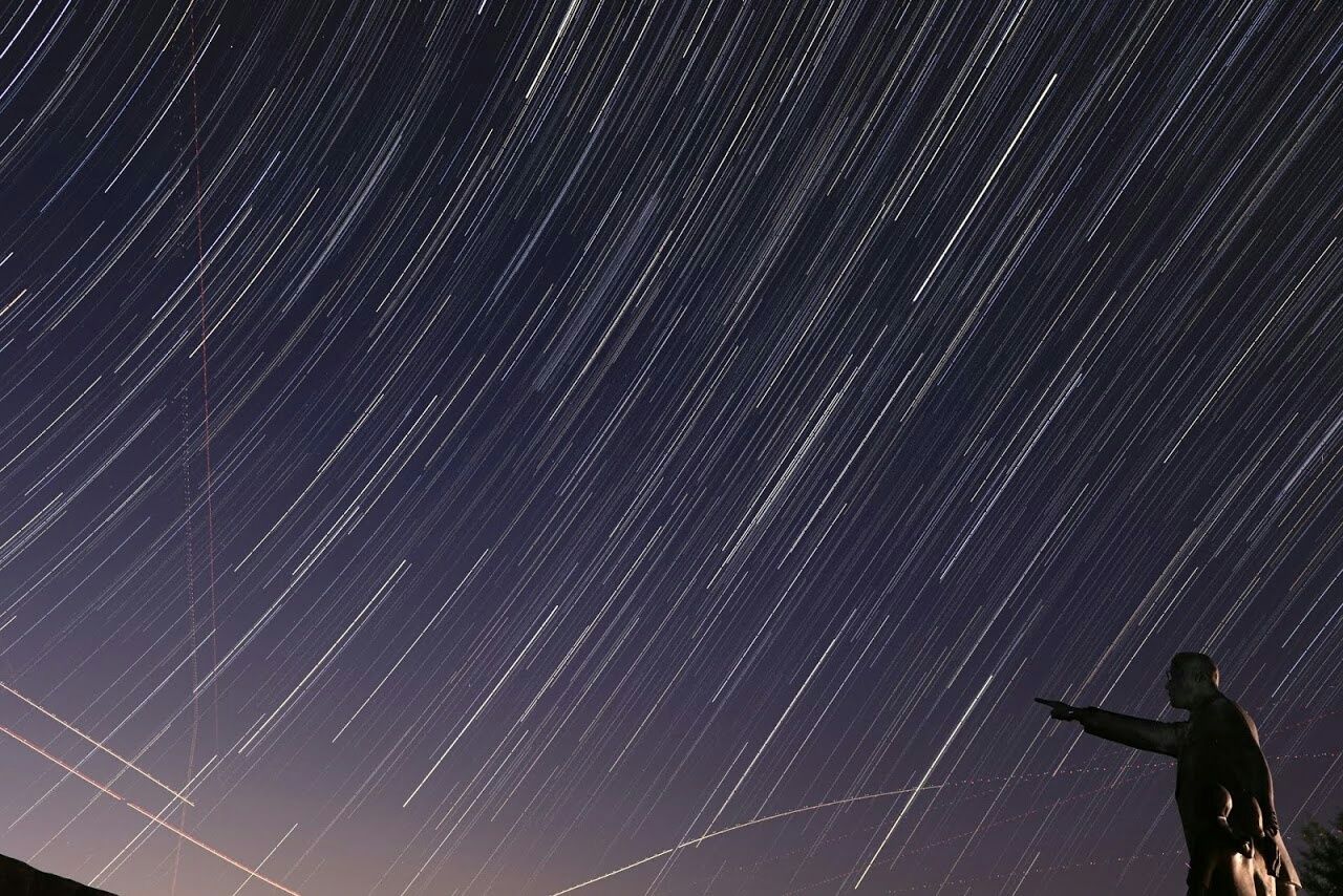 Low angle view of male statue against star trails in sky at night