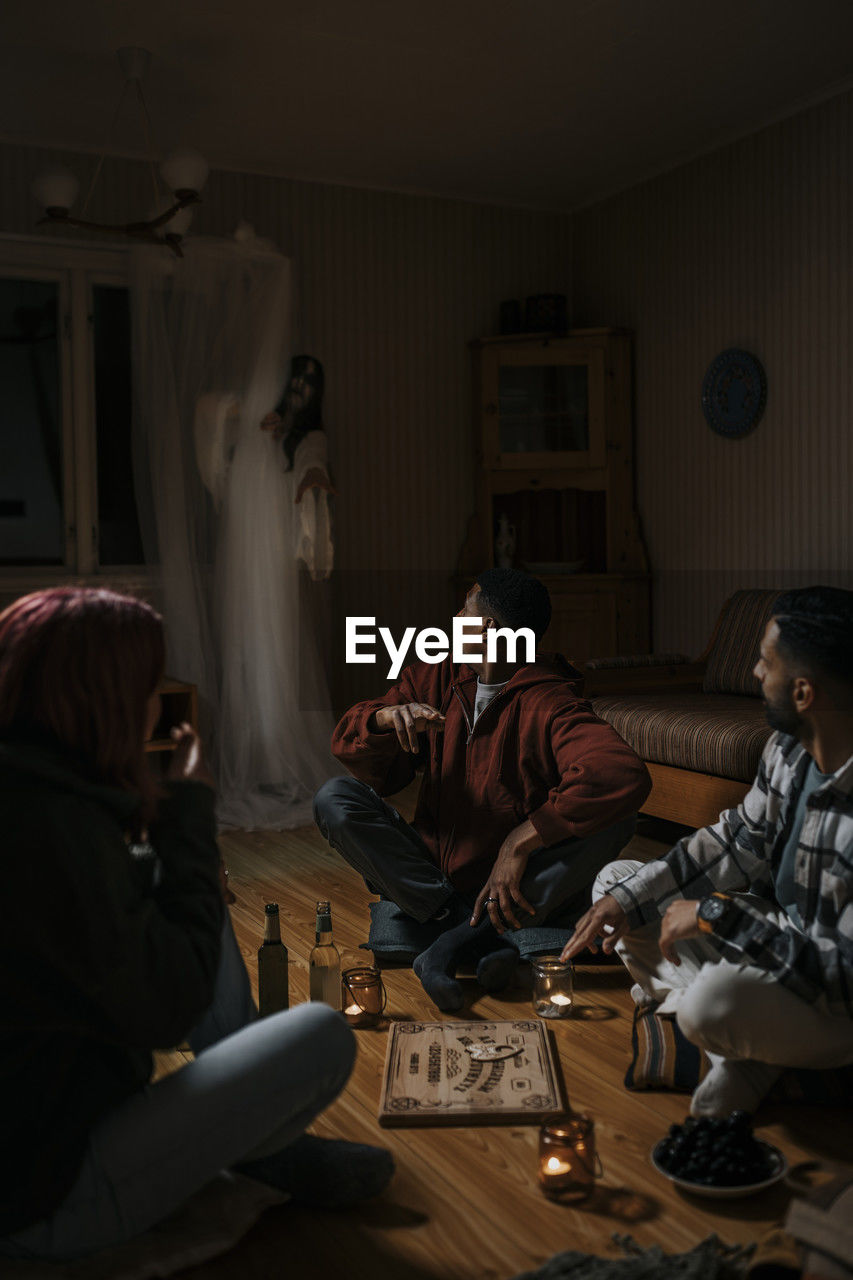 Terrified multiracial friends with ouija board looking at ghost in cabin