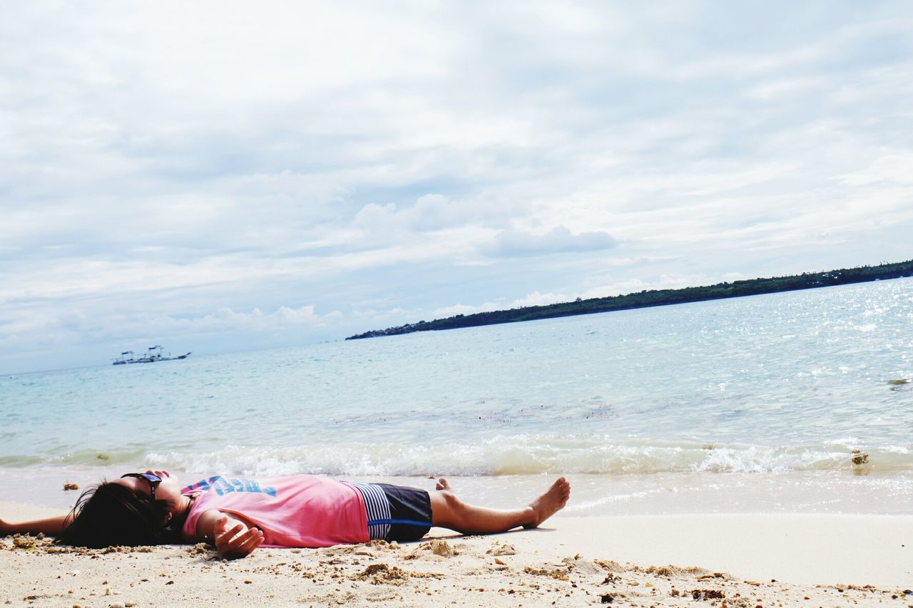 Woman lying at beach against sky