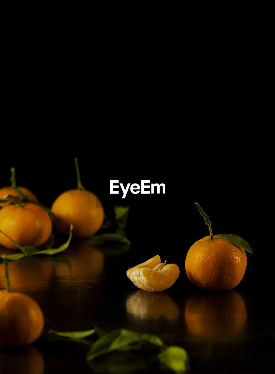 Still life of mandarins and leaves against black background