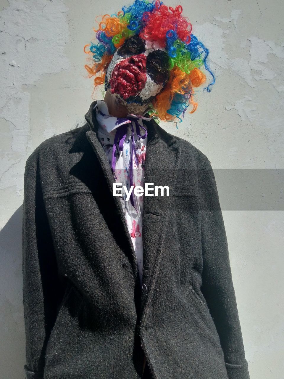 Young man in clown make up standing against wall