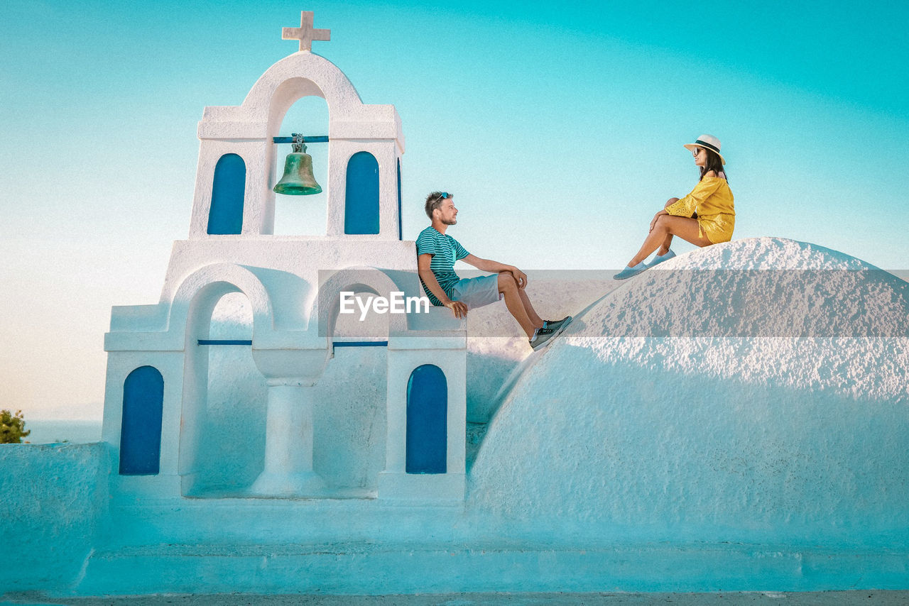 Couple talking while sitting by chapel against clear sky