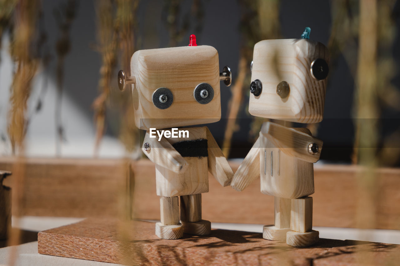 Two small wooden robots in the wooden jungle hold hands. friendship concept person