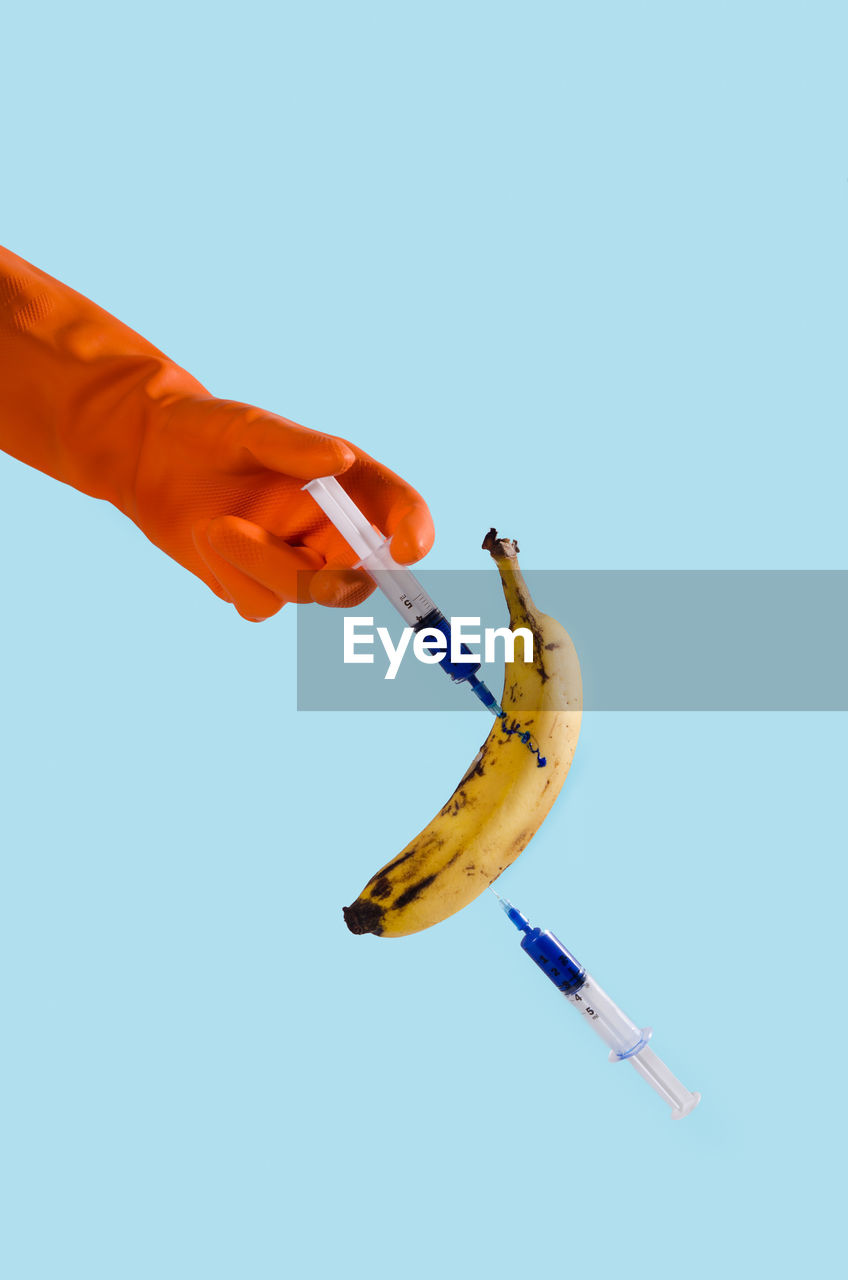 Cropped image of hand injecting banana against blue background