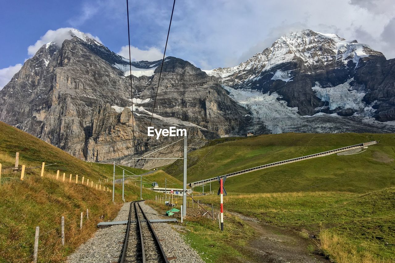 RAILROAD TRACK BY SNOWCAPPED MOUNTAINS AGAINST SKY